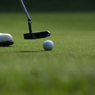 Close-up of a golf ball on the green, with a putter head and a player's shoe at Golf de Saint-Roman.