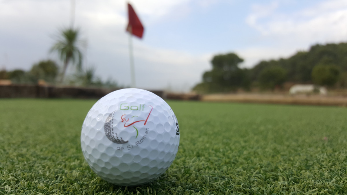 Close-up of a golf ball resting on the green at Golf de Saint-Roman, with the hole flag visible in the background.