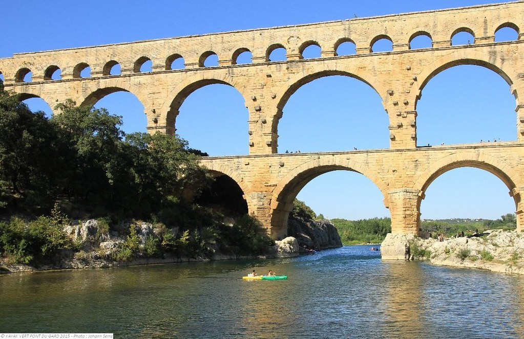 View of the Pont du Gard and its three tiers of stone arches, with a canoe on the Gardon River below the historic monument.