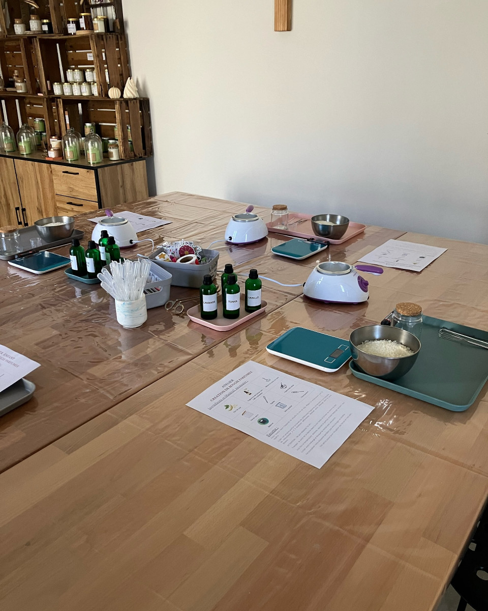 Large wooden table set up for a scented plant-based candle-making workshop in Bellegarde, with scales, containers, small bottles and instruction sheets.
