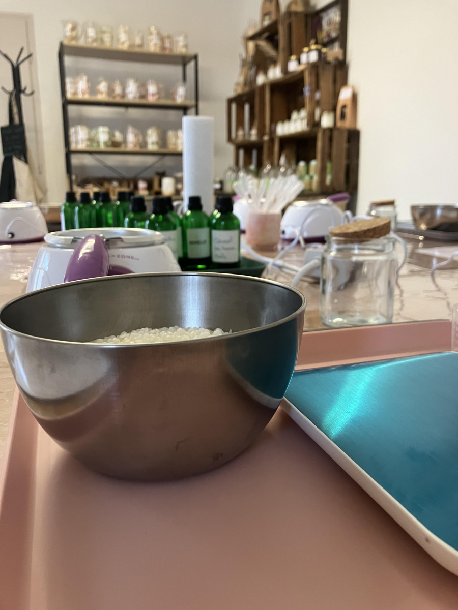 Metal bowl containing plant-based wax flakes on a workshop table, with a glass jar, small bottles and candle-making equipment in the background in Bellegarde.
