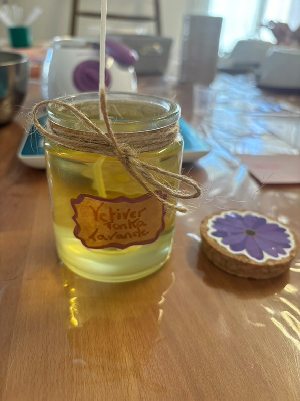 Plant-based candle scented with lavender, tonka bean and vetiver, displayed in a glass jar decorated with a label and twine, on a wooden table during a candle-making workshop in Bellegarde.