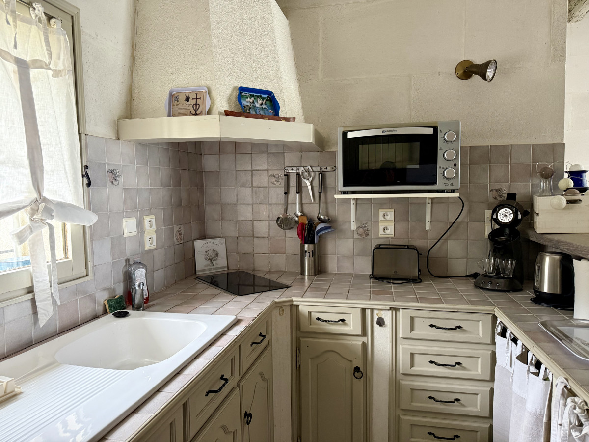 Cuisine équipée du gîte Le Nid d’Amour avec évier sous la fenêtre, meubles clairs, plaques de cuisson, hotte, four à micro-ondes et petit électroménager.