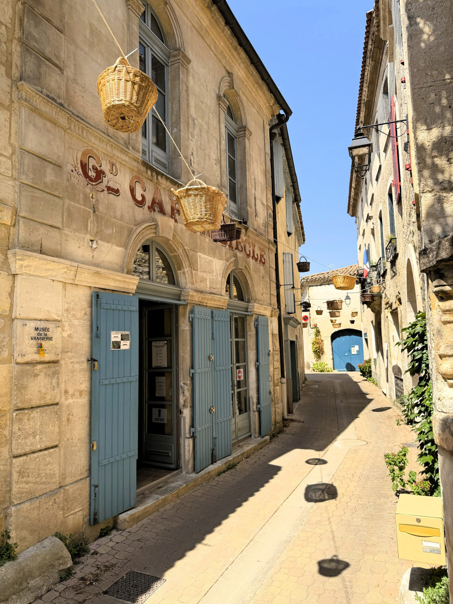 Street in Vallabrègues with hanging wicker baskets outside the former 19th-century Grand Café, now home to the Basketry Museum.