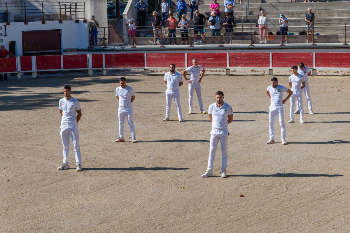 Plusieurs raseteurs en tenue blanche répartis sur la piste sablonneuse des arènes de Beaucaire, avec des spectateurs dans les gradins.