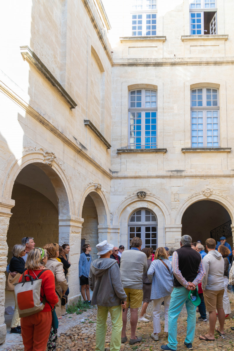 Groupe de visiteurs dans la cour pavée de l'hôtel de Clausonnette à Beaucaire, entourée d'arcades en pierre et de fenêtres anciennes.