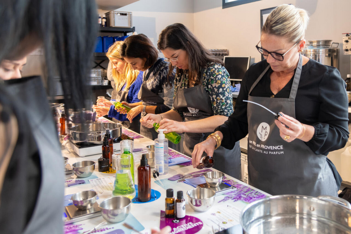 Participants preparing a nourishing lavender cream during a handmade cosmetics workshop at Un Mas en Provence in Bellegarde, gathered around a table with bottles, bowls and preparation utensils.