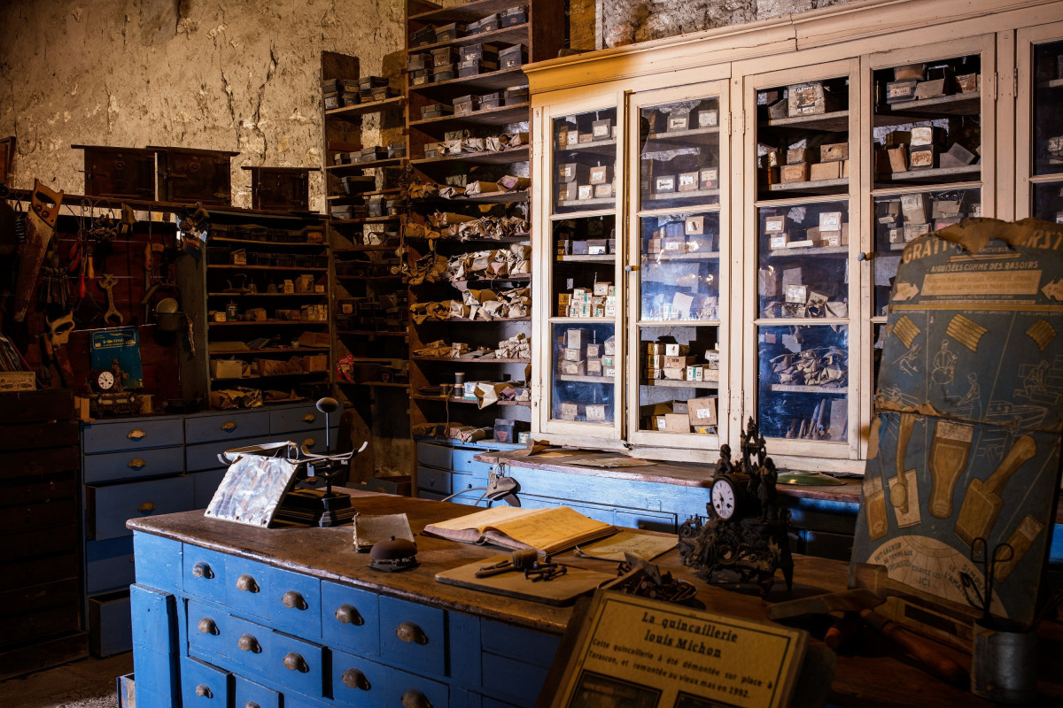 Interior of a historic workshop at Le Vieux Mas, with blue drawer cabinets, display cases, shelves and numerous objects on display.