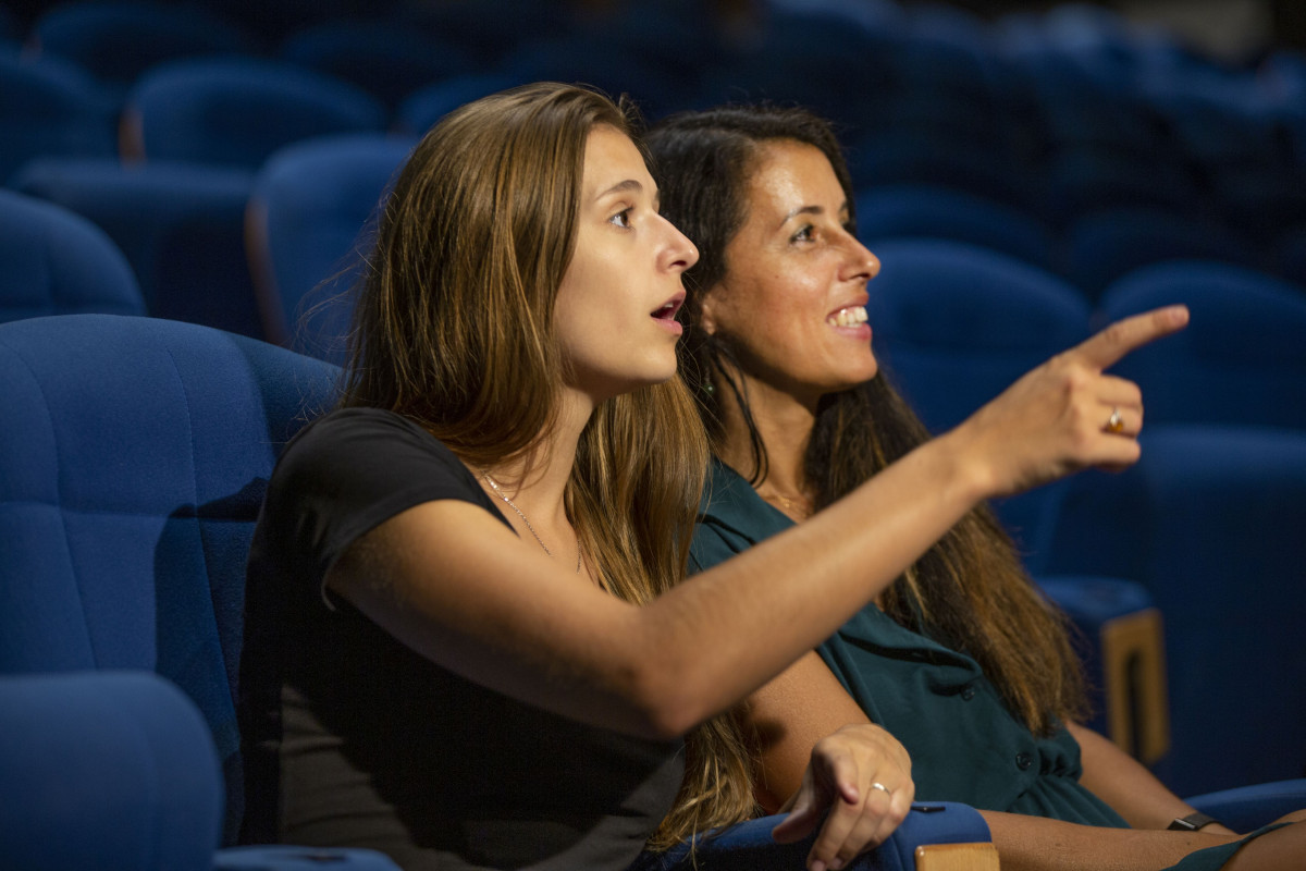 Two visitors seated in blue cinema chairs at the Pont du Gard cinema, with one of them pointing towards something ahead.