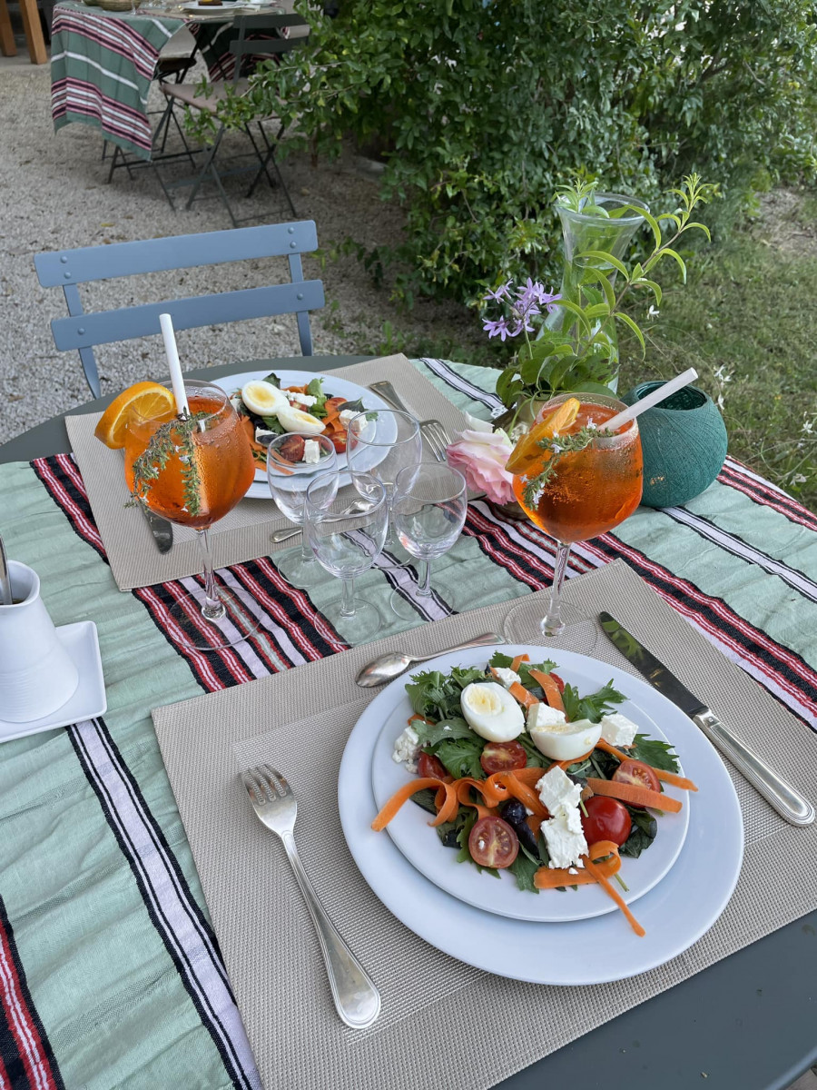 Outdoor dining table at Domaine des Clos with two plates of mixed salad, colourful dishes served in glasses, drinking glasses and a striped tablecloth.