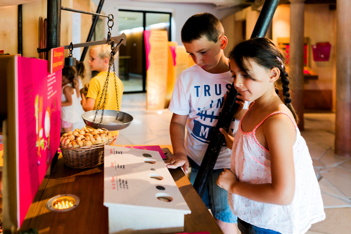 Two children examining an educational display featuring a balance scale and hands-on objects in the Pont du Gard Ludo area.