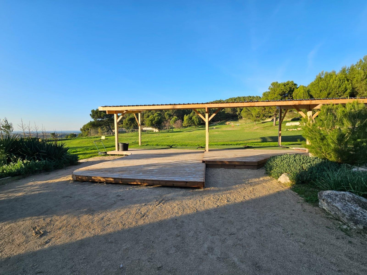 Exterior view of the covered driving range at Golf de Saint-Roman, with its long wooden structure, practice platforms and surrounding green spaces.