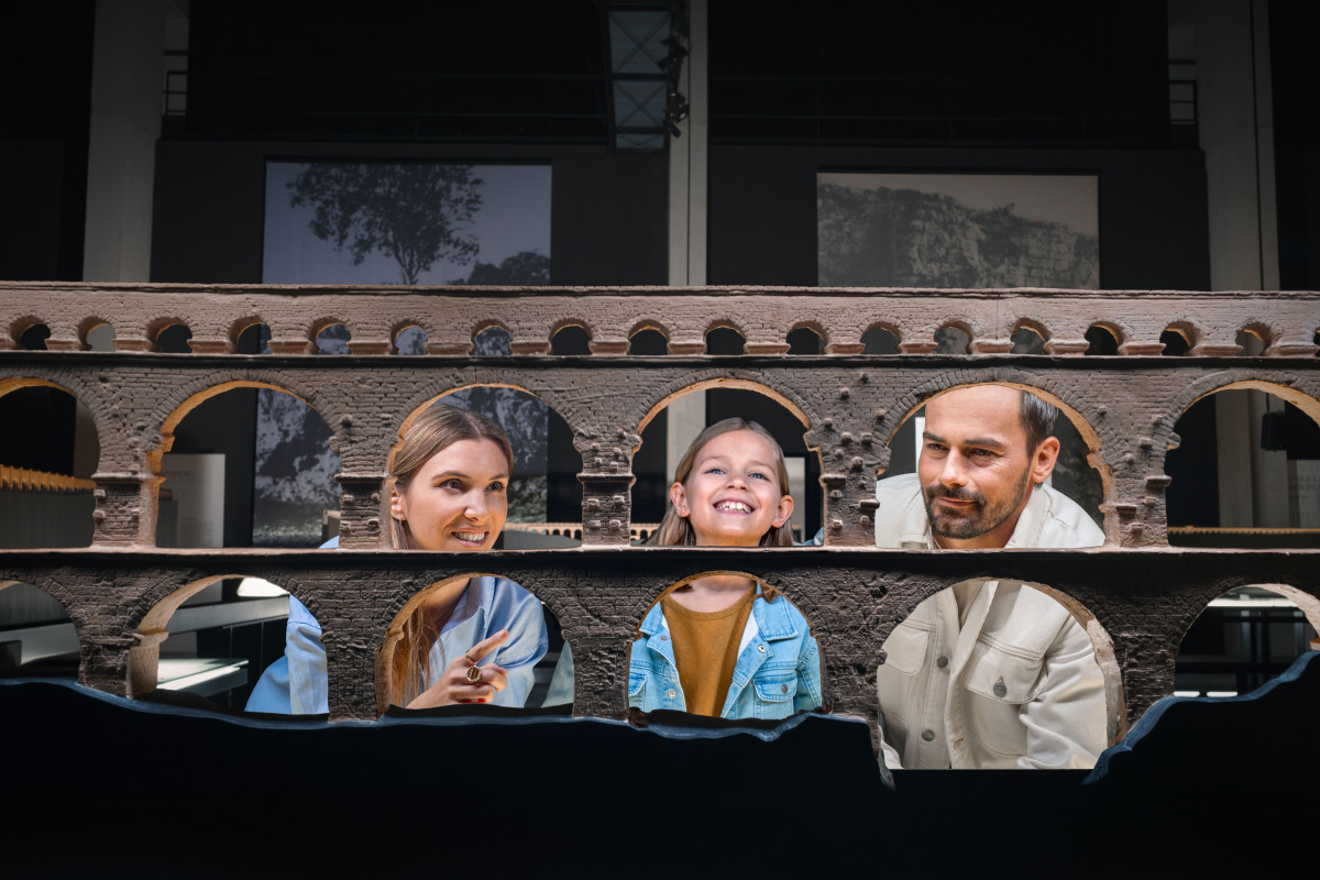 Two children and an adult smiling as they explore a model of the Roman aqueduct arches at the Pont du Gard Museum.