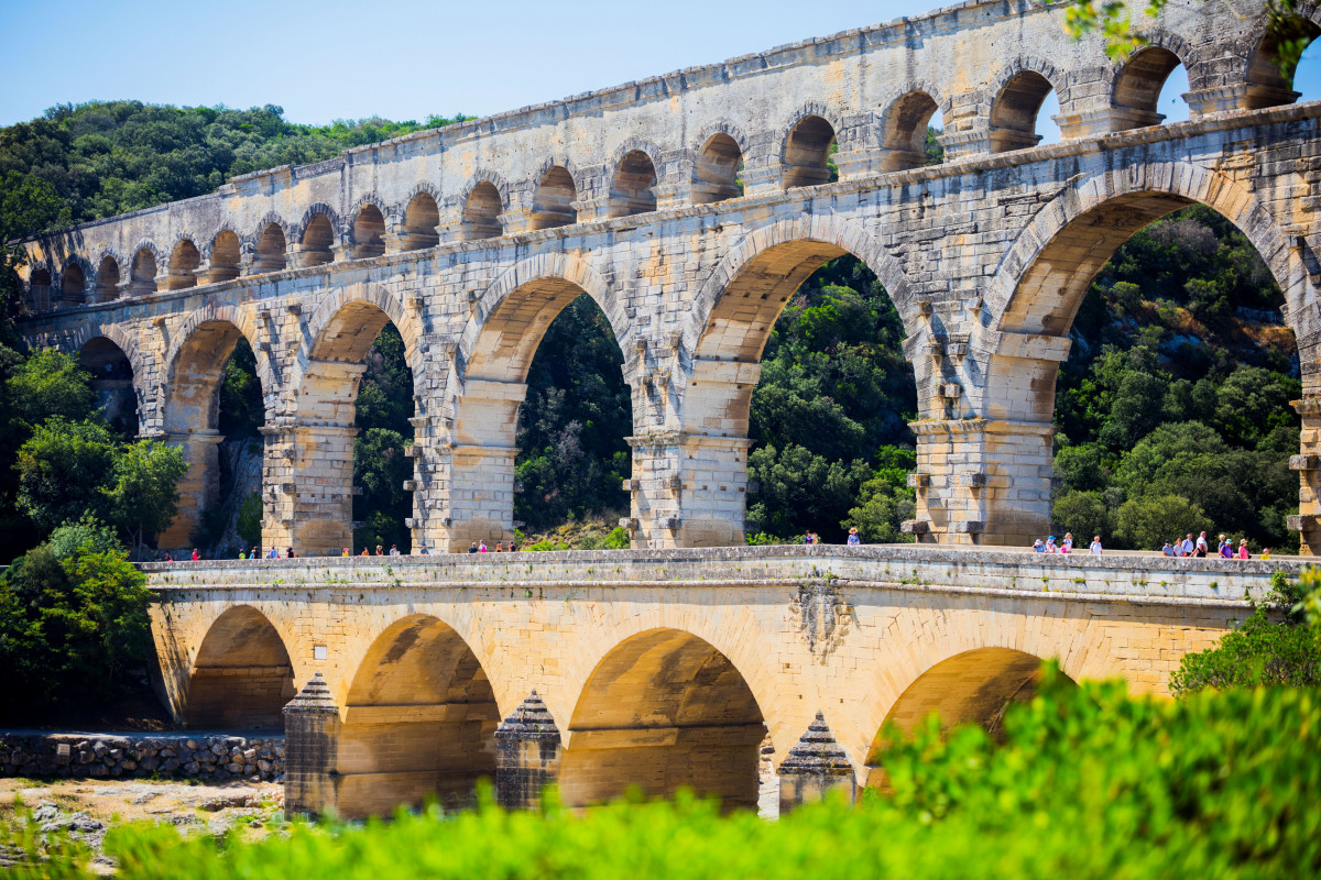 Close-up view of the three tiers of arches of the Pont du Gard Roman aqueduct, with visitors on the monument and vegetation in the foreground.