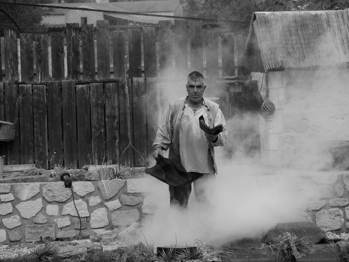 A performer stands in a stone-walled courtyard surrounded by thick smoke during a show at Le Vieux Mas.