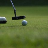 Close-up of a golf ball on the green, with a putter head and a player's shoe at Golf de Saint-Roman.
