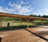 View of the practice area at Golf de Saint-Roman, featuring a covered wooden structure, platforms and a player practising on a golf mat.