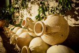 Row of terracotta amphorae with circular openings, arranged against a stone wall beneath foliage at Mas des Tourelles in Beaucaire.