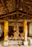 Old wine press with a wooden mechanism and ropes, positioned between large wooden posts beneath a timber roof at Mas des Tourelles in Beaucaire.