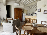 Pièce de vie du gîte Le Nid d’Amour à Vallabrègues avec table à manger ronde en bois, chaises, canapé gris, cuisine ouverte et poutres apparentes.