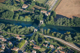 Aerial view of the old suspension bridge at Fourques crossing the Petit Rhône, with tree-lined riverbanks, nearby houses and farmland.