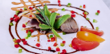 Assiette gastronomique de l'Auberge Amandin présentant une pièce de viande tranchée, des tomates rouges et jaunes, des herbes fraîches et une sauce disposée en cercle.