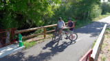 Two cyclists with their mountain bikes stopped on a paved path bordered by trees and railings during a full-day cycling outing offered by Kayak Vert.