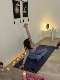 Participant practising a seated yoga pose with one arm raised on a mat in a room decorated with candles and wall hangings, illustrating a yoga session offered at Domaine Pierre-Feu in Jonquières-Saint-Vincent.