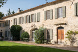 Stone façade of Domaine des Clos with shuttered windows, wooden doors, climbing plants and a lawn in the foreground.
