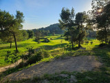 Elevated panoramic view of the Golf de Saint-Roman course, with green fairways, pine trees and sunlit wooded hills.