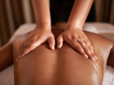 Close-up of a massage therapist's hands massaging the back of a person lying on a treatment table, illustrating the Relaxing Escape for Two at Domaine des Clos.