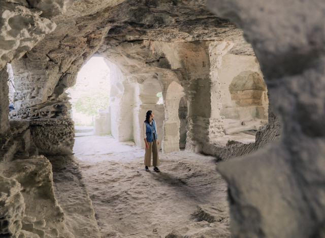 Saint-Roman Abbey – Exploring the Rock-Cut Interior Visitor inside a rock-cut chamber at Saint-Roman Abbey, with arches and openings letting in natural light.