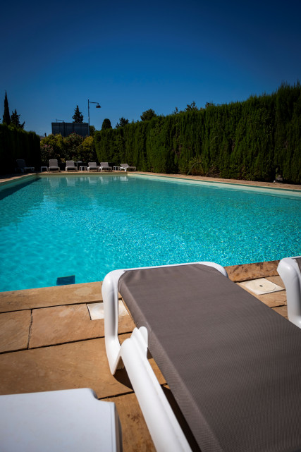 Hôtel Les Vignes Blanches – Swimming Pool Outdoor swimming pool at Hôtel Les Vignes Blanches, bordered by a tall green hedge, with sun loungers beside the water.