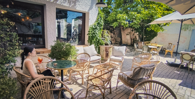 Hôtel Les Vignes Blanches – Outdoor Lounge Terrace at Hôtel Les Vignes Blanches with rattan chairs and tables, parasols, plants and a person seated in the outdoor lounge area.