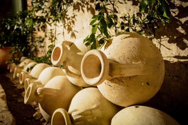 Row of terracotta amphorae with circular openings, arranged against a stone wall beneath foliage at Mas des Tourelles in Beaucaire.