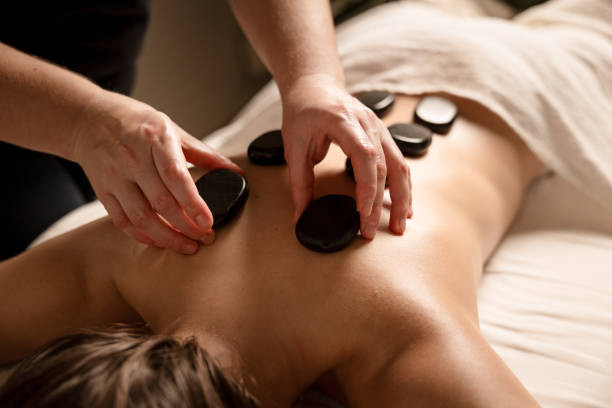 Close-up of a hot stone massage, with a practitioner placing smooth black stones on the back of a person lying face down on a massage table.